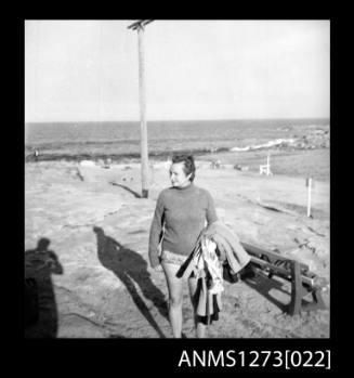 A man standing on a beach, holding a jacket