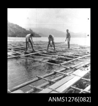 Three people standing on a pearl production raft on Pearl Island