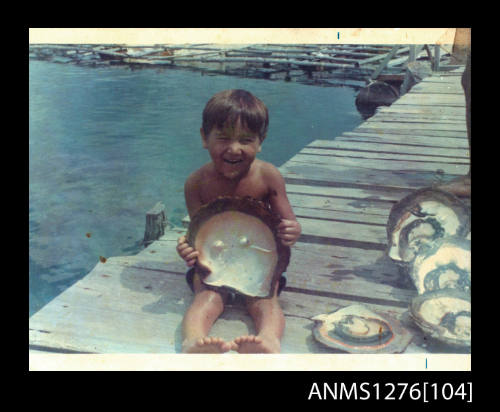 Boy sitting on a wharf holding a large pearl shell with two blister pearls on Pearl Island