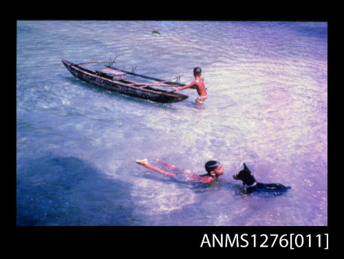 35mm colour transparency of two young boys, presumably two of Denis George's sons, one holding onto a canoe, and the other swimming with a black dog