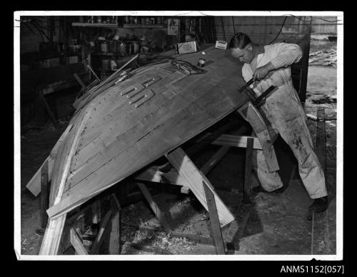 Print depicting workman clamping planking to a small wooden boat under construction