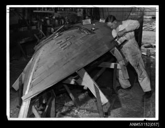 Print depicting workman clamping planking to a small wooden boat under construction