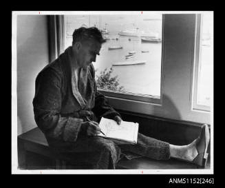 British boat designer Uffa Fox wearing paisley-patterned dressing gown, seated on window sill seat