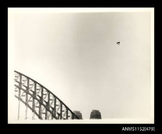 The hang-glider passing over an arch and the top of two pylons of the Sydney Harbour bridge