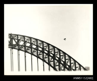 The hang-glider passing over an arch and the top of one pylon of the Sydney Harbour bridge