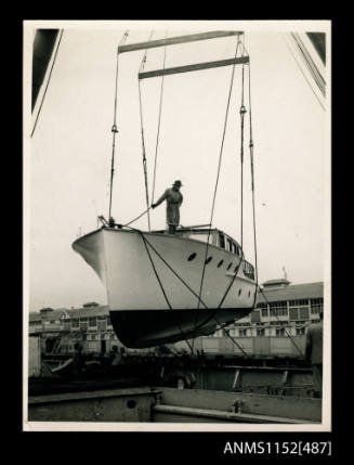 The cabin cruiser unnamed suspended from crane over hatch of cargo ship