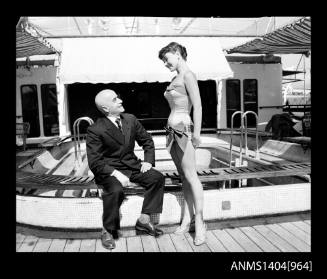 Photographic negative of a swimsuit model posing by a pool on a ship with a man in a suit