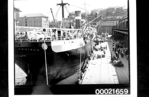 Wharf labourers using derricks to load bales of wool and crates into the holds of SS CANADIAN CRUISER 