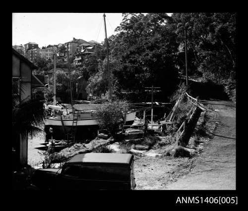 Negative depicting several moored boats, a sandstone retaining wall and several apartment buildings in the background, taken from the river bank