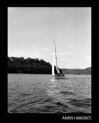 Negative depicting a sail boat underway on the harbour with a tree covered headland in the background