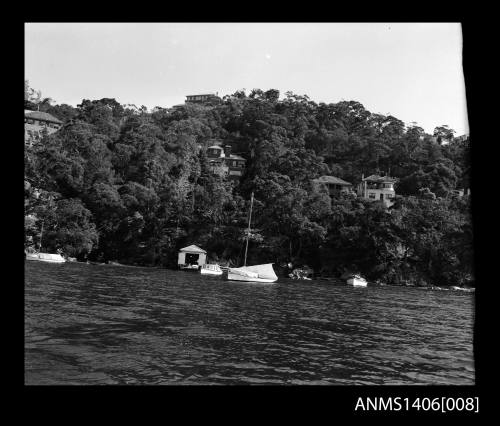 Negative depicting several boats near a shore and boat house with several homes built on the hill behind