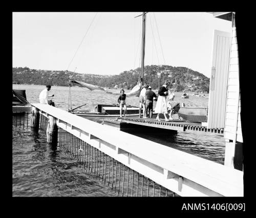 Negative depicting a sail boat docked with a small jetty, where several people are gathered