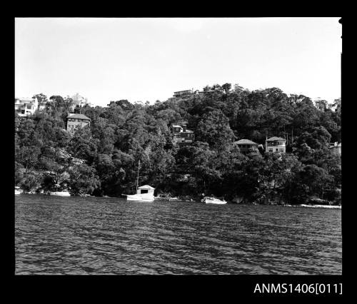 Negative depicting three white boats near a shore and a boat house with several homes built on the hill behind