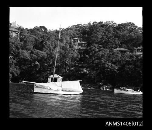 Negative depicting two boats near a shore and a boat house with several homes built on the hill behind