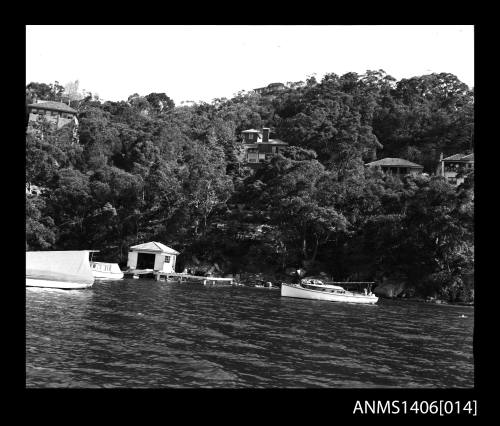 Negative depicting three white boats on the river, near a boat house, with several homes built on the hill behind