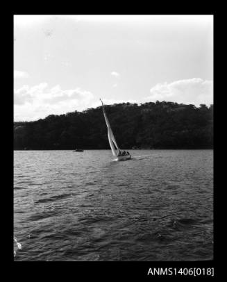 Negative depicting a yacht underway, from portside bow, with a five person crew and in the background is a tree covered headland