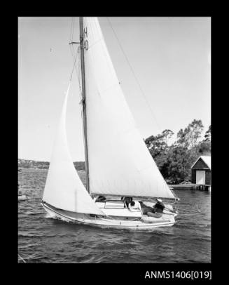 Negative depicting a yacht underway, from portside, with a five person crew and headlands with houses are visible in the background