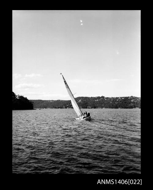 Negative depicting a yacht underway, shown from the stern, with a five person crew and headlands with houses are visible in the background