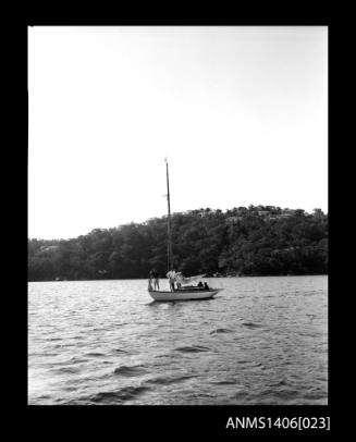 Negative depicting a sail boat, from portside, with a five person crew on a river and a headland with houses is visible in the background