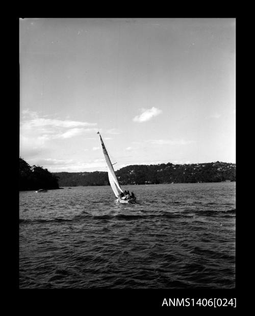 Negative depicting a yacht underway, from stern, with a five person crew and headlands with houses are visible in the background