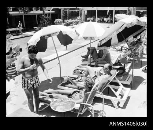 Negative depicting several people around a hotel pool, on beach lounge chairs under umbrellas