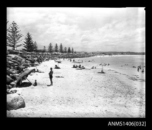 Negative depicting beach goers on the sand with umbrellas and people entering the surf