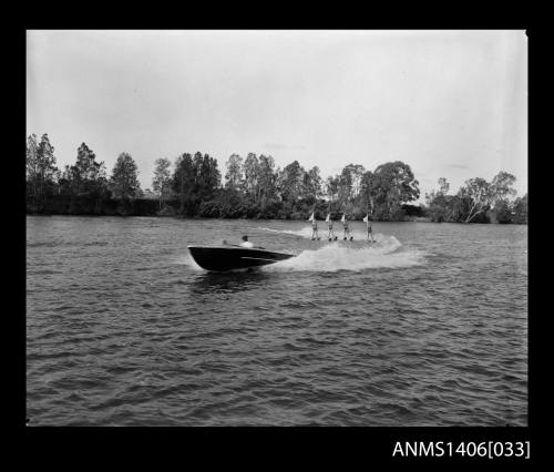 Negative depicting a motorboat, shown from portside bow and four water-skiers carrying flags, on a river