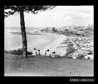 Negative depicting a group of four having a picnic on a hill, under a pine tree, overlooking a beach and nearby houses