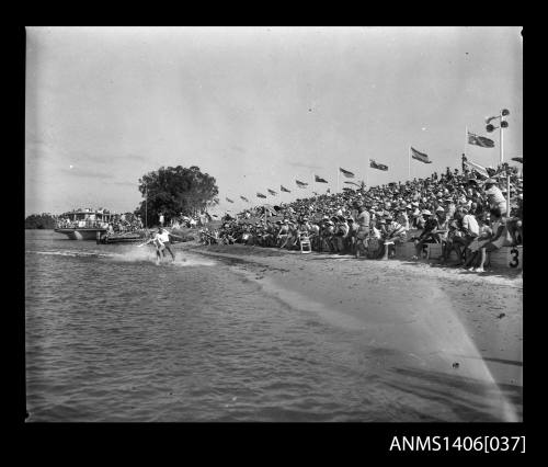 Negative  depicting two water-skiers in the water, entertaining the crowd on the river bank