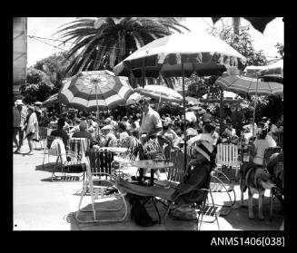 Negative depicting a crowd of people around cafe tables, under umbrellas