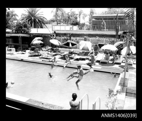 Negative depicting several people jumping into and around a hotel pool with beach lounge chairs and umbrellas nearby