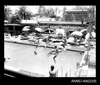 Negative depicting several people jumping into and around a hotel pool with beach lounge chairs and umbrellas nearby