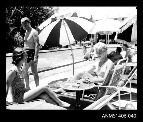 Negative depicting two women in bathingsuits, sitting in beach lounge chairs beside a pool