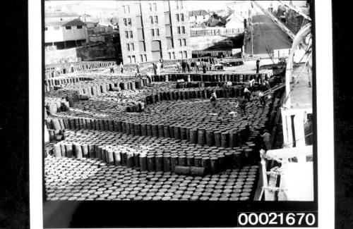 Wharf labourers unloading and stacking cargo of drums from steamship