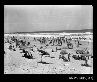 Negative depicting beach goers on the sand with umbrellas and towels as well as people entering the surf