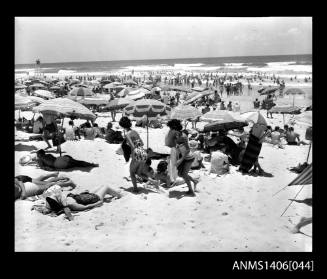 Negative depicting beach goers on the sand with umbrellas and towels as well as people entering the surf