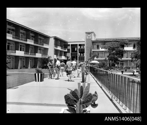 Negative depicting a family group walking beside the pool, out the front of the motel buildings