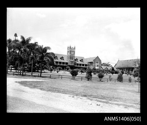 Negative depicting a large mansion type building with a wooden fence and a palm lined drive
