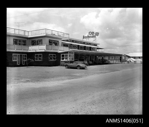 Negative depicting the front reception of a two storey motel with a driveway and multiple carports