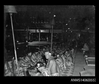 Negative depicting guests at a large banquet dinner by torch light