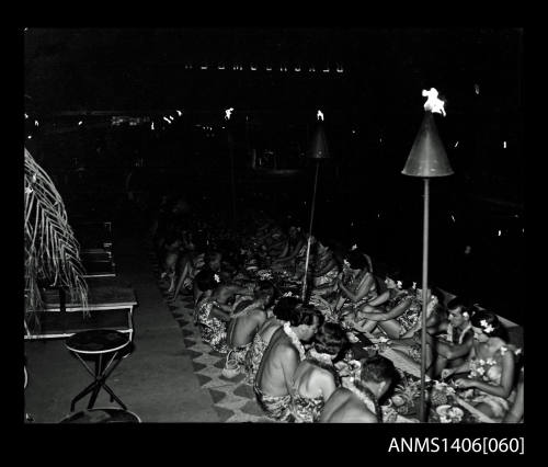 Negative depicting guests at a large banquet dinner by torch light