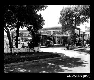 Negative depicting the front of a hotel/serviced apartments with a small picket fence and several trees as well as umbrellas