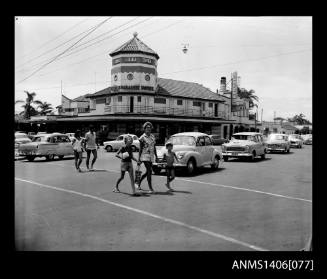 Negative depicting the Surfers Paradise Hotel and a couple and woman with two children crossing at an intersection