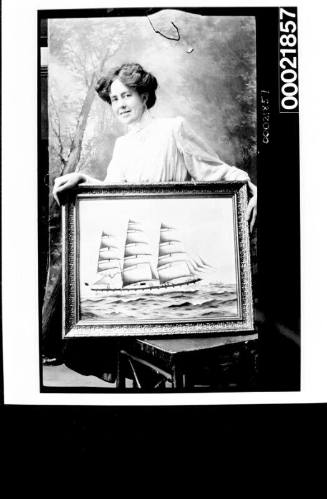 Woman seated holding framed photograph of fully rigged ship
