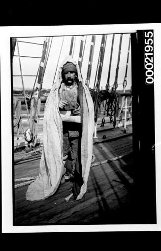 Crewman grinding pepper under a sailcloth on the deck of a ship