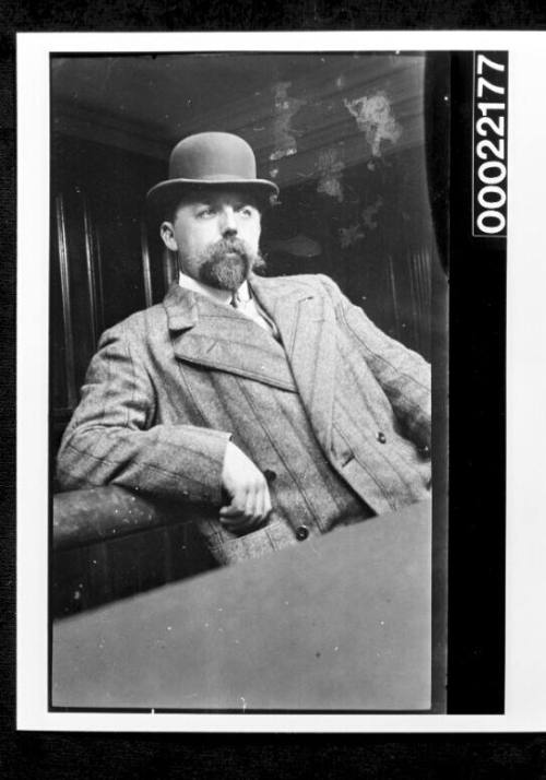 A study in beards and moustaches,  man wearing bowler hat and leaning against chair