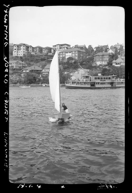 Yachting World Cadet dinghy on Sydney Harbour with Sydney ferry in distance.