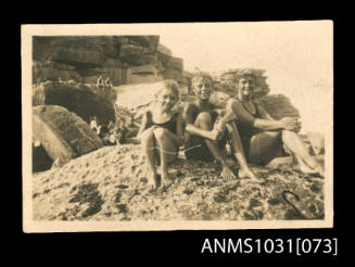 Black and white photograph of Beatrice Kerr and two young boys sitting on a rocky section of beach in their swim suits