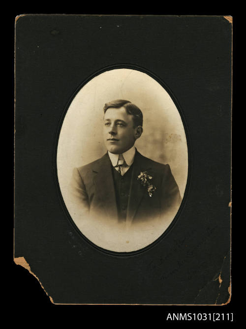 Black and white portrait photograph of a young man wearing a jacket, waistcoat and tie, with a flower in his pocket