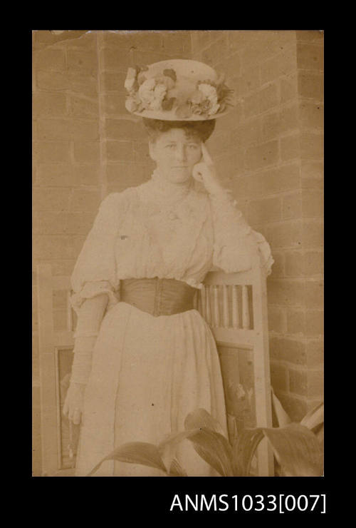 Photograph of a woman wearing large floral hat and white dress